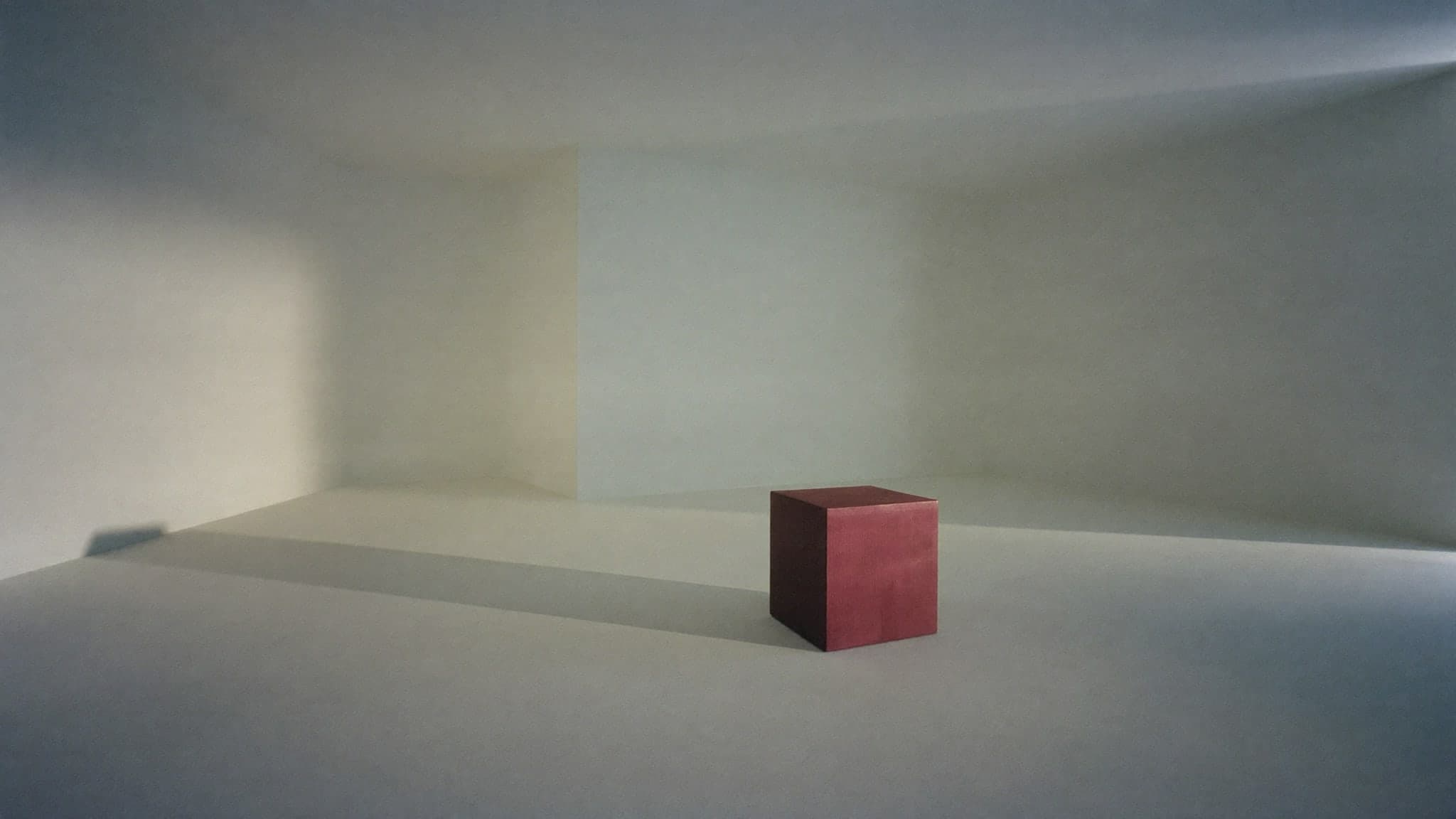 Una sala enorme y vacía con un único cubo burdeos pequeño apoyado en el suelo.